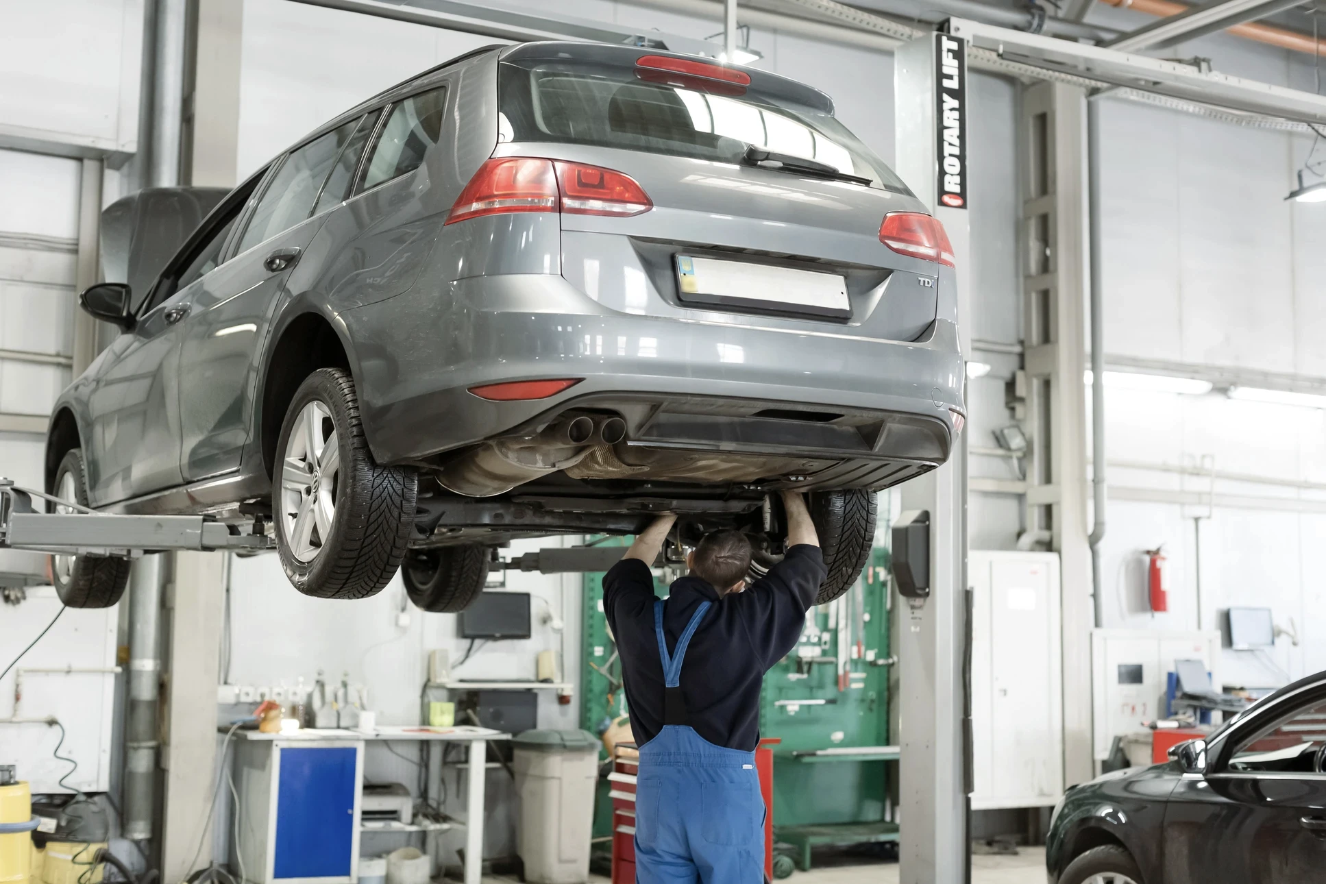 Atelier automobile professionnel avec mécanicien travaillant sous véhicule surélevé sur pont élévateur hydraulique